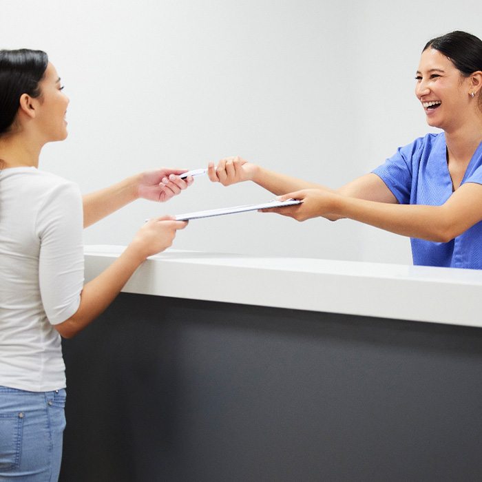 Smiling dental assistant handing patient form