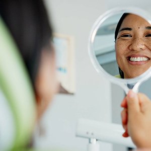 Woman smiling at her reflection in a handheld mirror