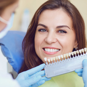 Cosmetic dentist holding veneers in front of a woman's smile