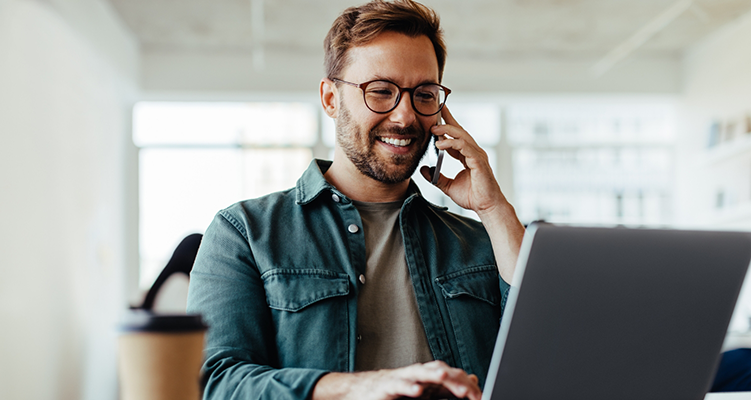 Smiling man talking on the phone while using laptop to request a dental appointment in Wilmington