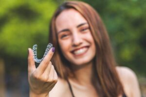 Woman smiling and holding up her clear aligners