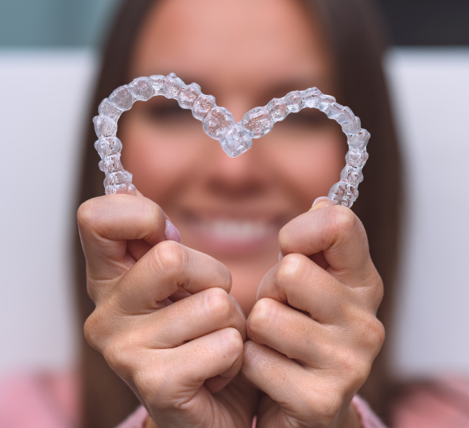 Woman holding Invisalign clear aligners in heart shape