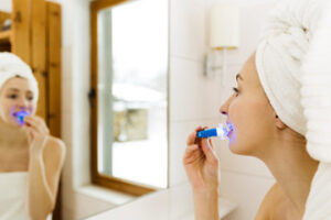 Woman looking into mirror while whitening teeth at home
