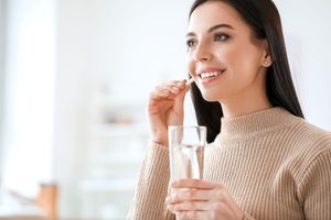 Woman holding white pill and glass of water